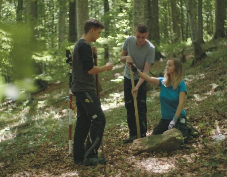 drei Auszubildende Vermessungstechniker*innen messen im Wald
